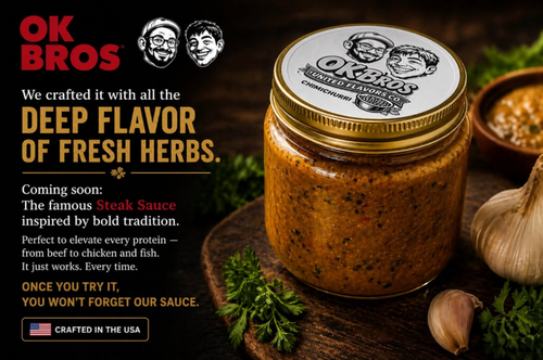 A jar of Ok Bros. steak sauce on a rustic dark wooden surface with garlic, herbs, and a small bowl of sauce.